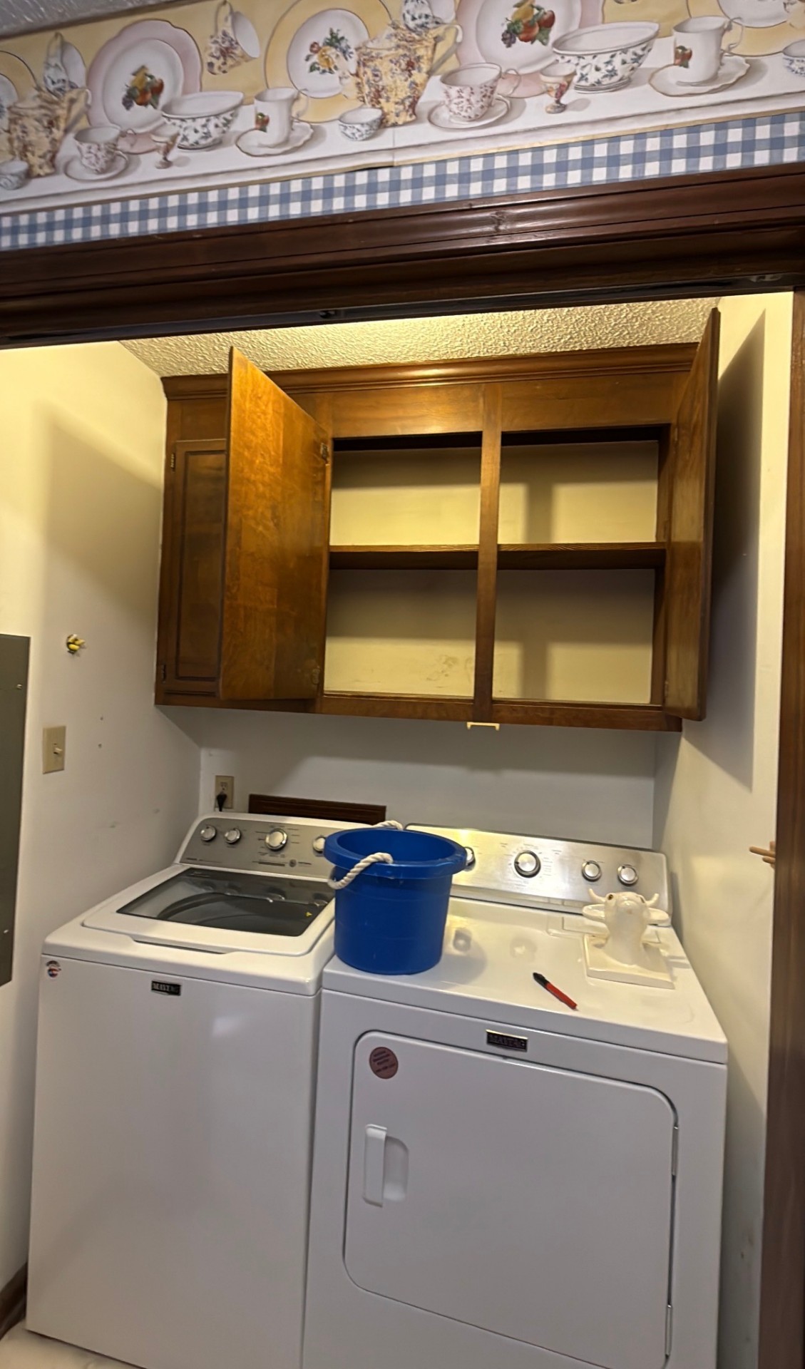 Before: Before photo of a laundry nook with a dark wood cabinet and dated wallpaper border — Laundry Nook Refresh, Cabinet Painting by CJC Remodeling