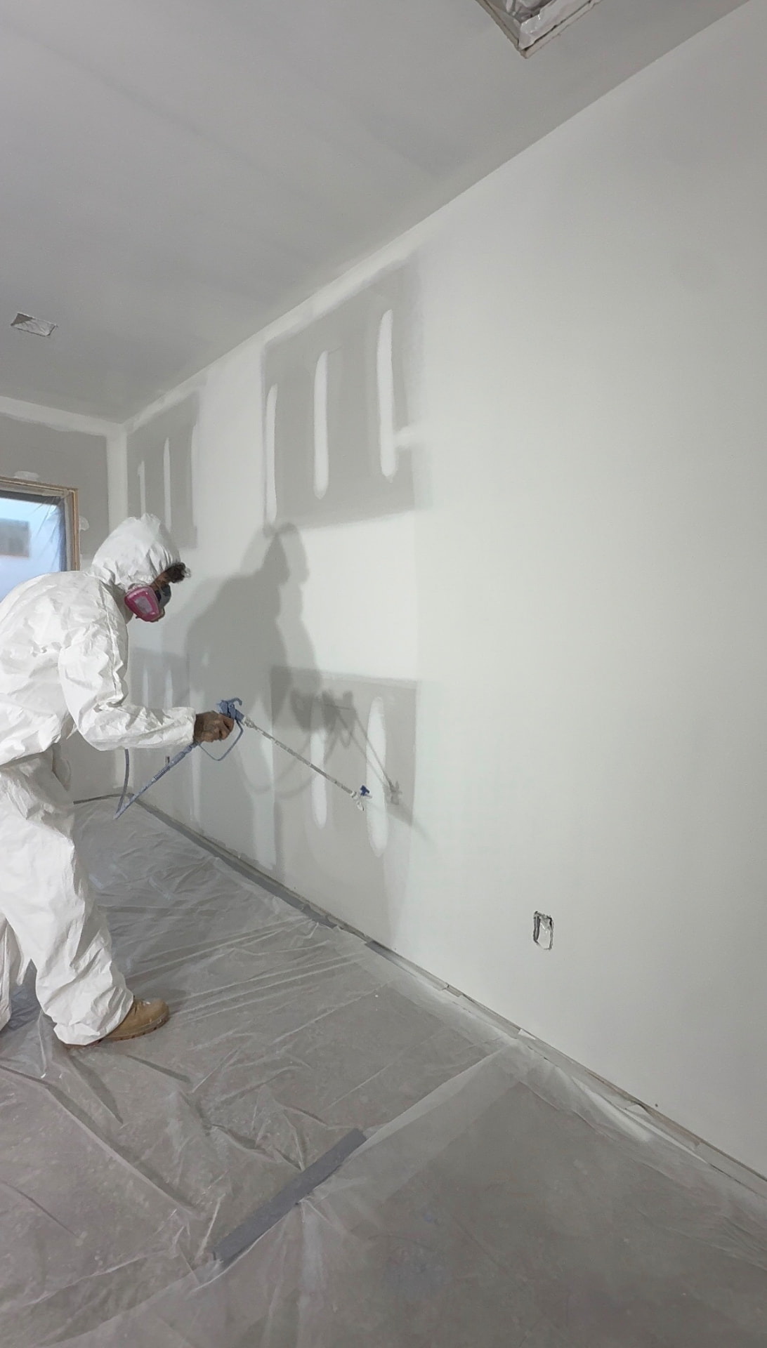 Spraying newly taped and floated drywall walls