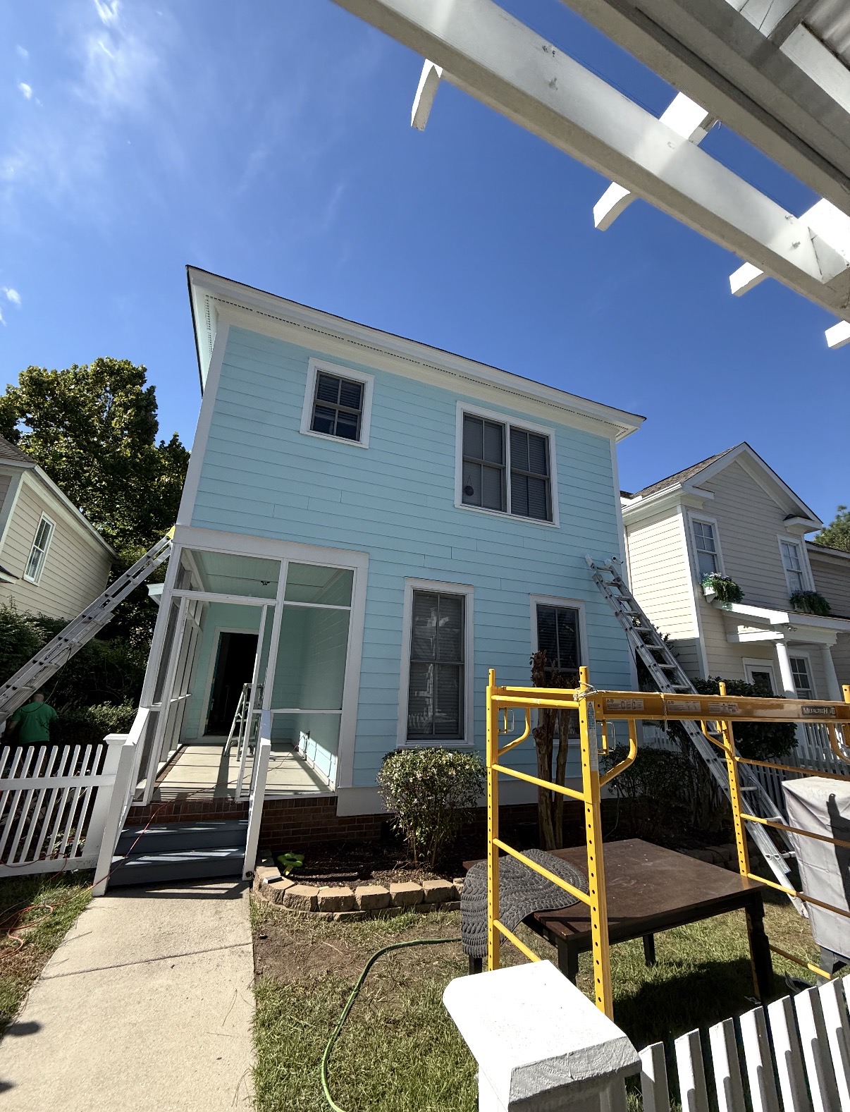 Rear of a light blue two-story home with a screened porch and scaffolding after exterior painting